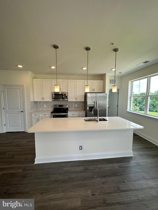 kitchen featuring a kitchen island with sink, hanging light fixtures, dark hardwood / wood-style floors, white cabinetry, and stainless steel appliances