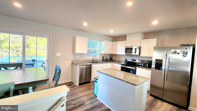 kitchen with sink, appliances with stainless steel finishes, light stone counters, white cabinets, and a kitchen island