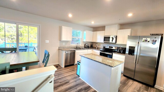 kitchen with appliances with stainless steel finishes, sink, white cabinets, a center island, and light stone countertops