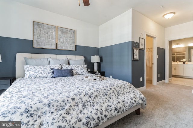 bedroom featuring ceiling fan, a walk in closet, connected bathroom, and light carpet