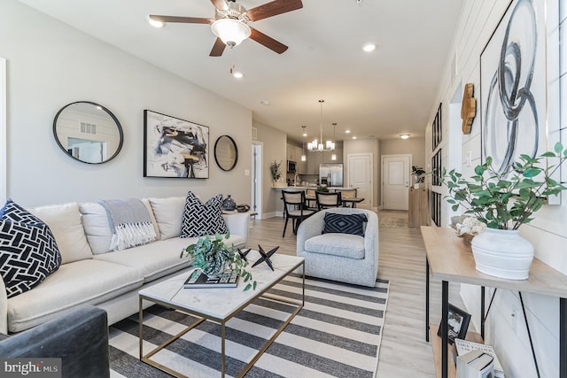 living room featuring ceiling fan with notable chandelier and light wood-type flooring