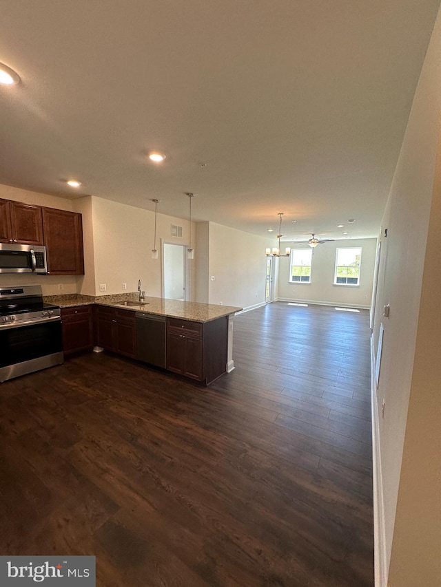 kitchen with appliances with stainless steel finishes, dark hardwood / wood-style floors, decorative light fixtures, sink, and light stone counters