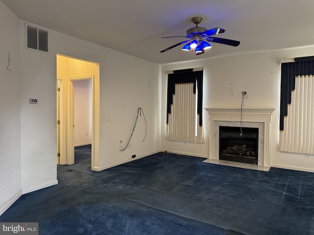 unfurnished living room featuring a premium fireplace, ceiling fan, and dark carpet