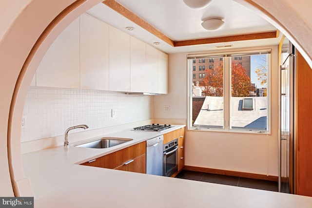 kitchen featuring decorative backsplash, appliances with stainless steel finishes, sink, dark tile patterned flooring, and white cabinets