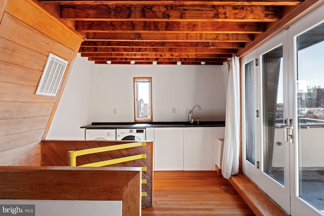 kitchen with wooden walls, beam ceiling, light hardwood / wood-style flooring, washer / clothes dryer, and white cabinetry