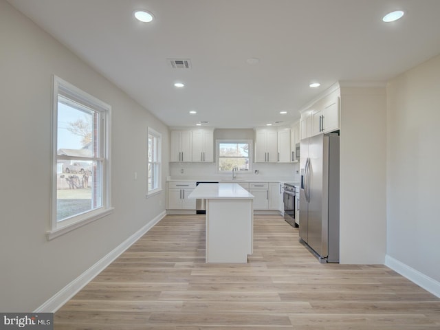 kitchen with white cabinets, light wood-type flooring, stainless steel appliances, and a kitchen island