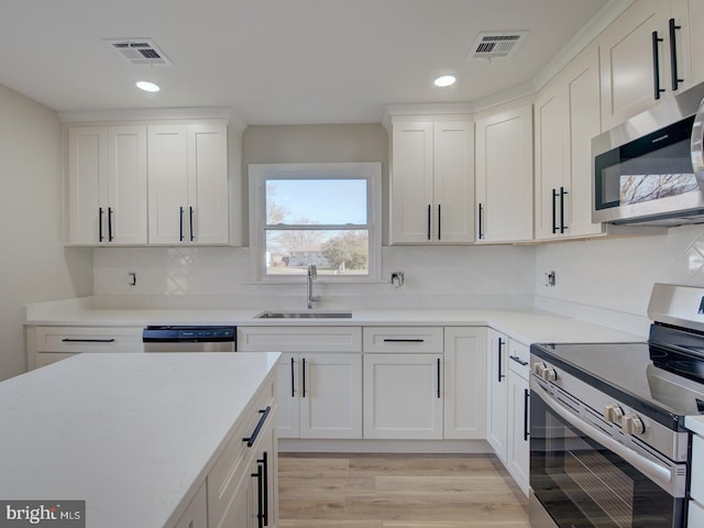 kitchen featuring white cabinets, sink, light hardwood / wood-style flooring, decorative backsplash, and stainless steel appliances