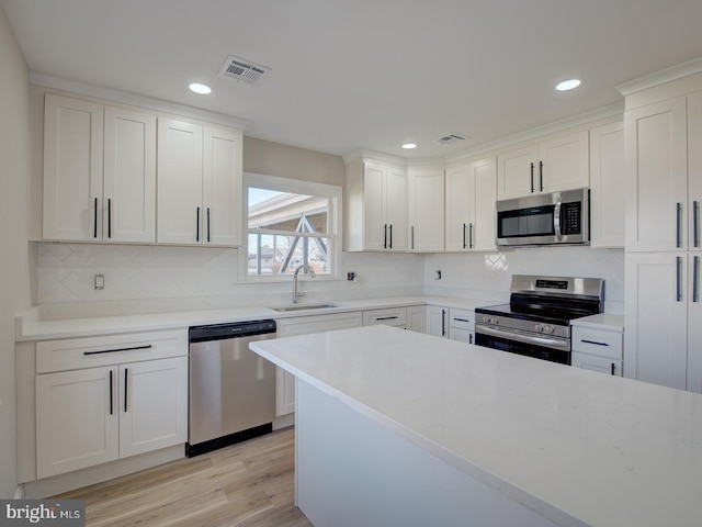 kitchen with white cabinets, appliances with stainless steel finishes, light wood-type flooring, and sink