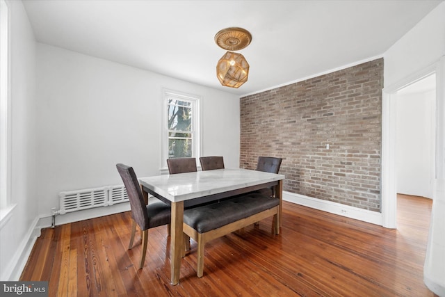 dining area with wood-type flooring and brick wall