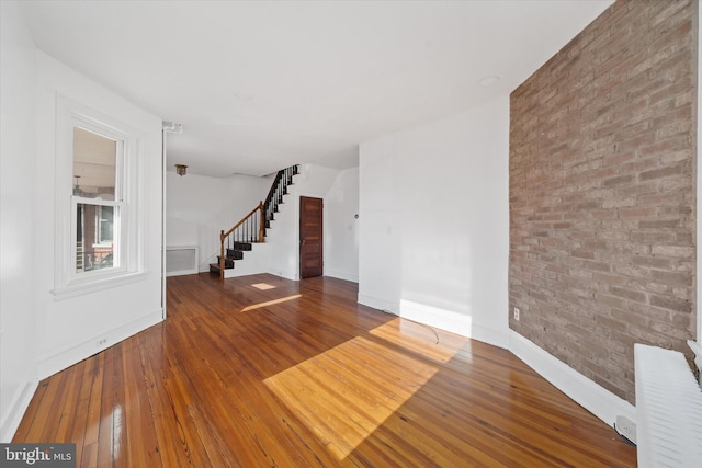 unfurnished living room featuring brick wall and hardwood / wood-style floors