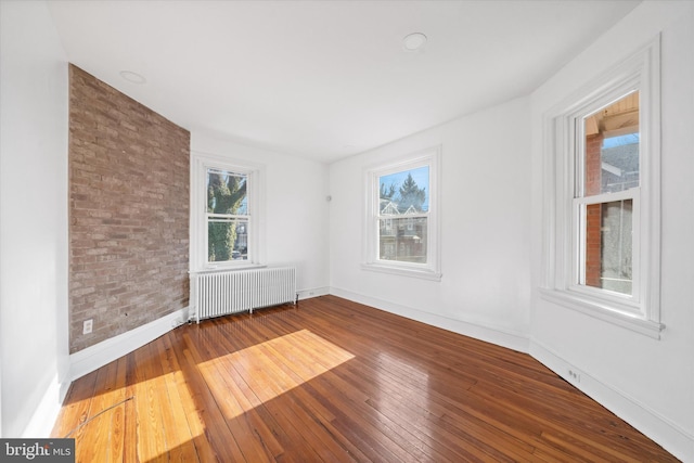 spare room with brick wall, radiator heating unit, and wood-type flooring