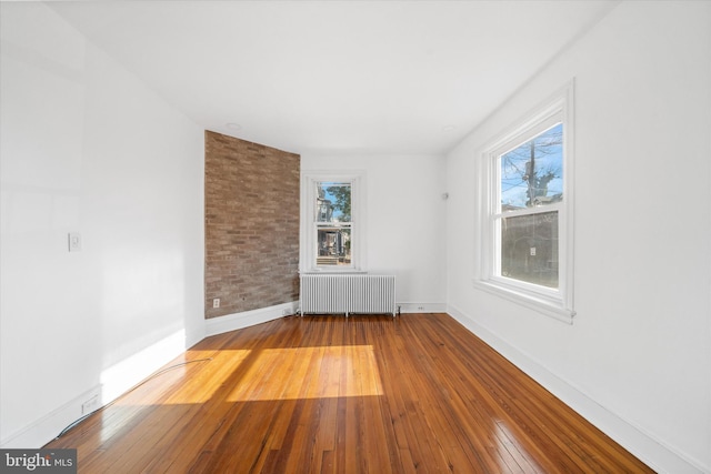 empty room with a healthy amount of sunlight, radiator heating unit, hardwood / wood-style floors, and brick wall