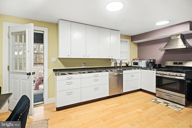 kitchen featuring wall chimney exhaust hood, white cabinetry, stainless steel appliances, and light hardwood / wood-style flooring