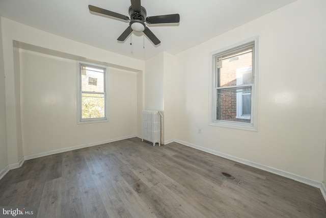 spare room featuring plenty of natural light, ceiling fan, wood-type flooring, and radiator heating unit