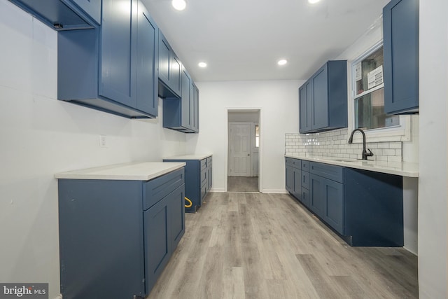 kitchen with decorative backsplash, blue cabinets, sink, and light hardwood / wood-style flooring