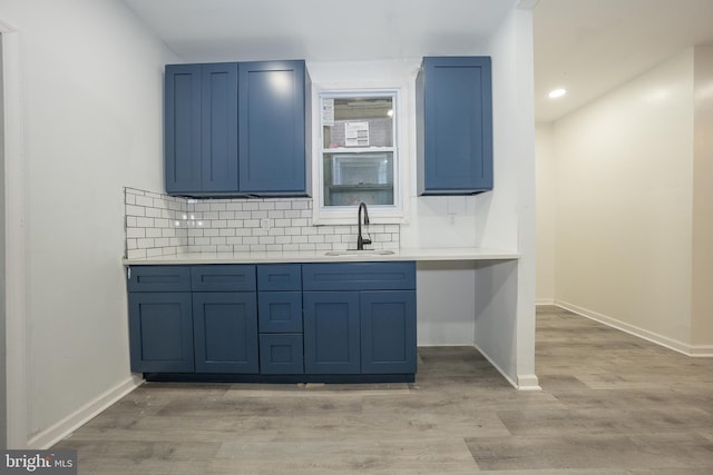 kitchen featuring blue cabinetry, light wood-type flooring, tasteful backsplash, and sink