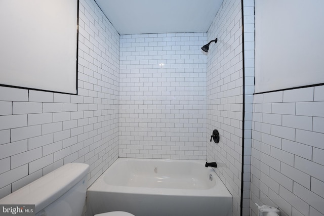 bathroom with tiled shower / bath, toilet, and tile walls