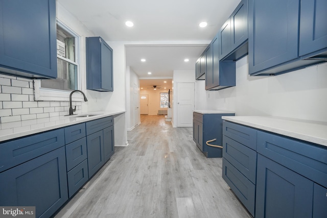 kitchen with decorative backsplash, light wood-type flooring, ceiling fan, sink, and blue cabinetry