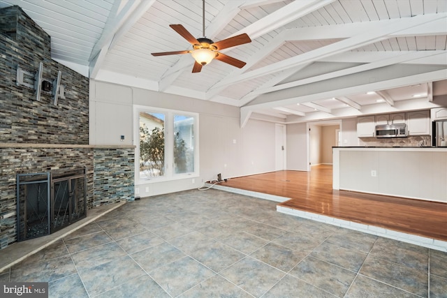 unfurnished living room with ceiling fan, tile patterned floors, a stone fireplace, and lofted ceiling with beams