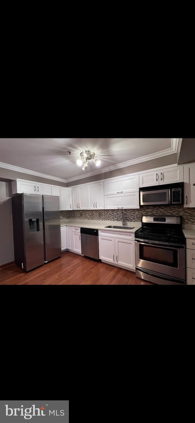 kitchen with appliances with stainless steel finishes, ornamental molding, sink, wood-type flooring, and white cabinetry