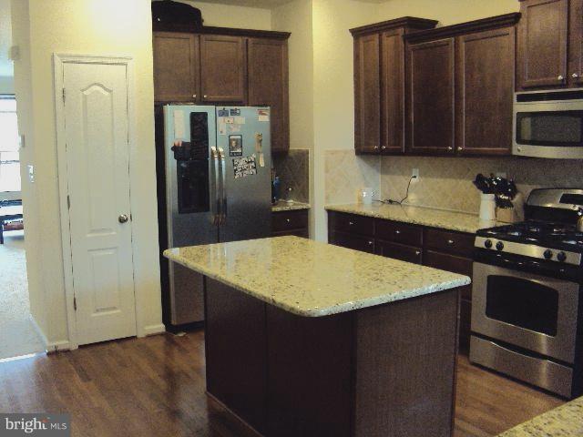 kitchen with light stone countertops, dark brown cabinetry, stainless steel appliances, dark hardwood / wood-style floors, and a kitchen island