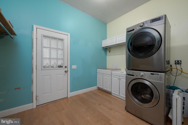 laundry room with light hardwood / wood-style floors, cabinets, and stacked washing maching and dryer