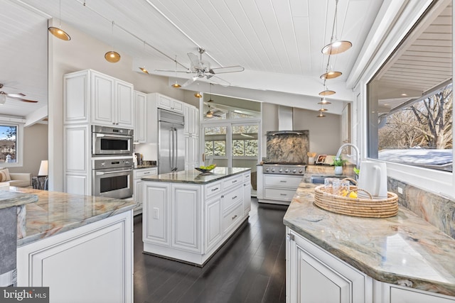 kitchen with appliances with stainless steel finishes, white cabinetry, hanging light fixtures, a kitchen island, and dark stone counters