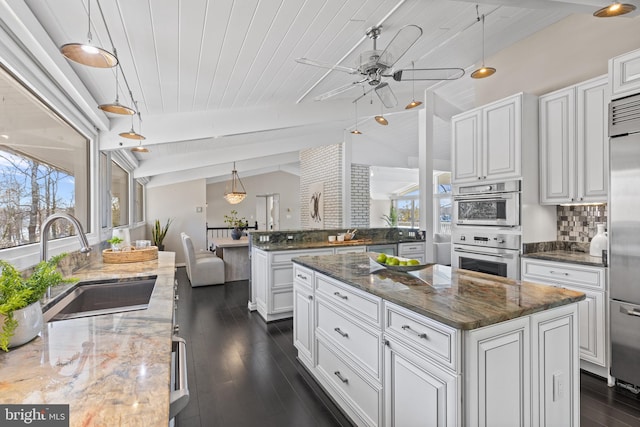 kitchen featuring pendant lighting, white cabinetry, sink, dark stone counters, and a center island