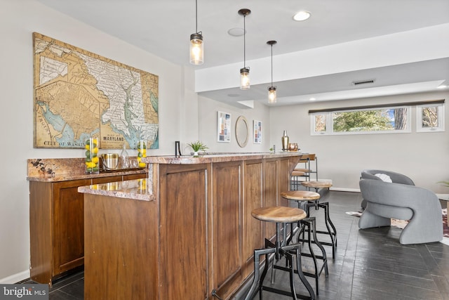 bar with light stone counters, decorative light fixtures, and dark hardwood / wood-style flooring