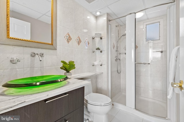 bathroom with toilet, tile walls, vanity, a shower with door, and backsplash