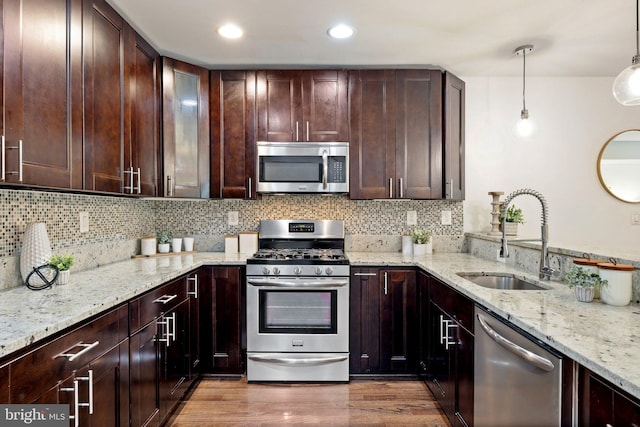 kitchen with light stone counters, stainless steel appliances, sink, wood-type flooring, and hanging light fixtures