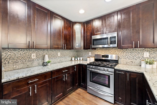 kitchen featuring decorative backsplash, light hardwood / wood-style floors, light stone counters, and appliances with stainless steel finishes