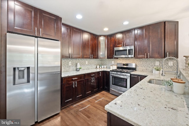 kitchen featuring light stone countertops, appliances with stainless steel finishes, decorative backsplash, sink, and light hardwood / wood-style floors