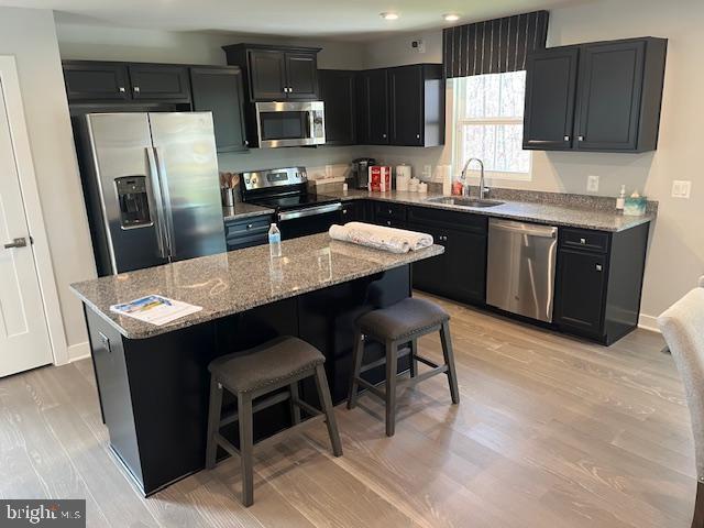 kitchen featuring a kitchen breakfast bar, stainless steel appliances, sink, light hardwood / wood-style flooring, and a kitchen island