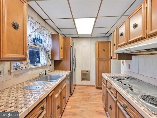 kitchen with sink, a drop ceiling, heating unit, light hardwood / wood-style floors, and appliances with stainless steel finishes