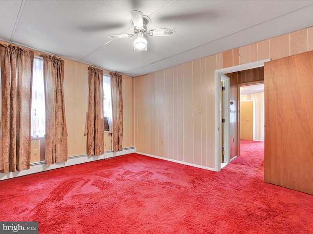 unfurnished room featuring carpet flooring, wood walls, ceiling fan, and a baseboard radiator