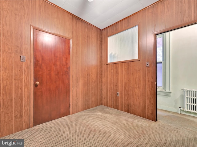 carpeted spare room featuring radiator heating unit and wooden walls