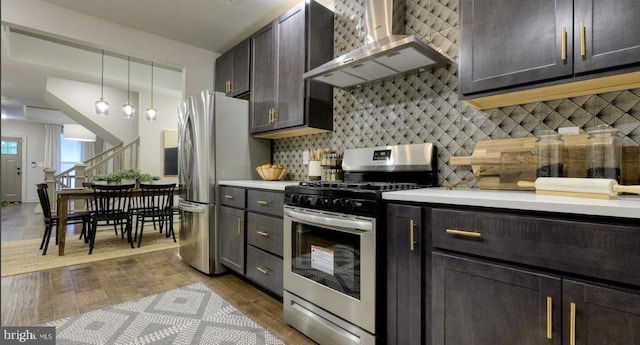 kitchen with pendant lighting, wall chimney exhaust hood, decorative backsplash, light wood-type flooring, and appliances with stainless steel finishes