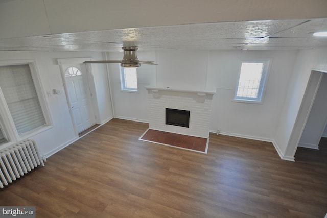 unfurnished living room with dark hardwood / wood-style flooring, radiator heating unit, and a brick fireplace