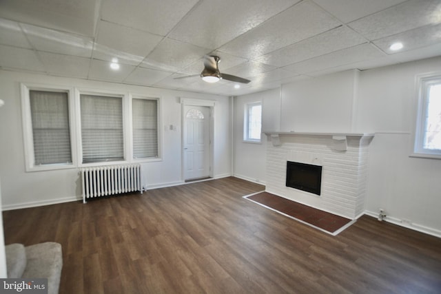 unfurnished living room featuring a wealth of natural light, dark wood-type flooring, radiator, and a brick fireplace