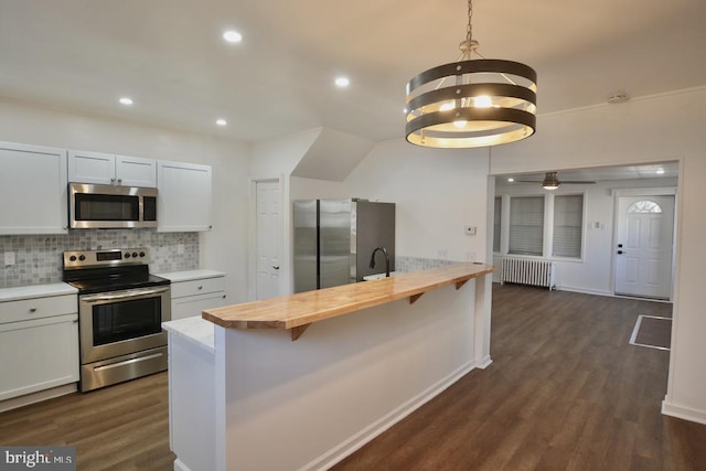 kitchen with wood counters, appliances with stainless steel finishes, dark wood-type flooring, white cabinets, and radiator heating unit