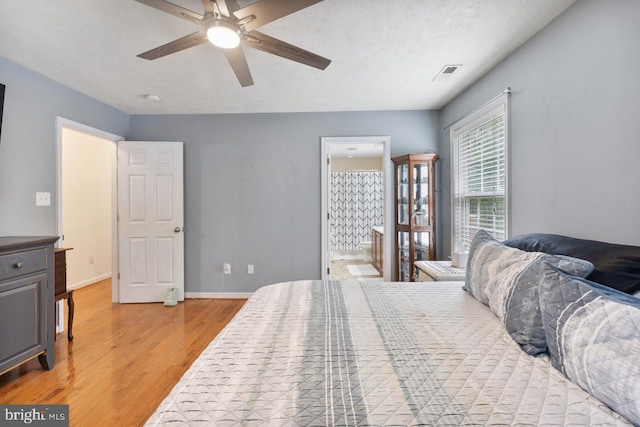 bedroom with ensuite bathroom, ceiling fan, light hardwood / wood-style floors, and a textured ceiling