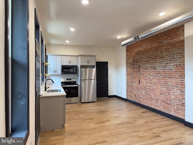 kitchen with brick wall, appliances with stainless steel finishes, light hardwood / wood-style floors, and sink