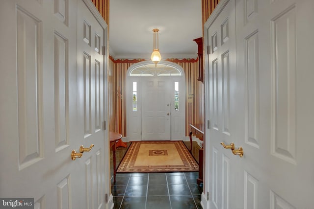 entryway with dark tile patterned floors and crown molding