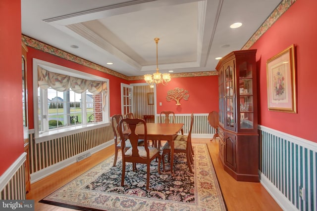 dining area featuring light wood-type flooring, a raised ceiling, and a notable chandelier