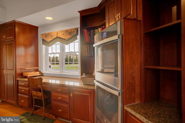 kitchen with double oven, light stone counters, hardwood / wood-style floors, and built in desk