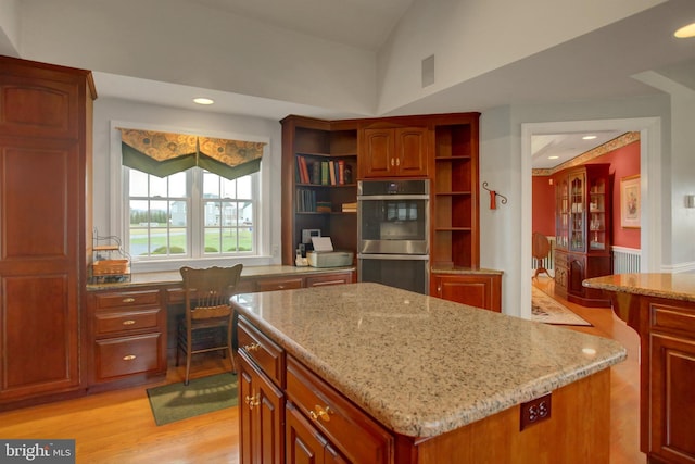 kitchen with a center island, lofted ceiling, built in desk, light hardwood / wood-style floors, and stainless steel double oven