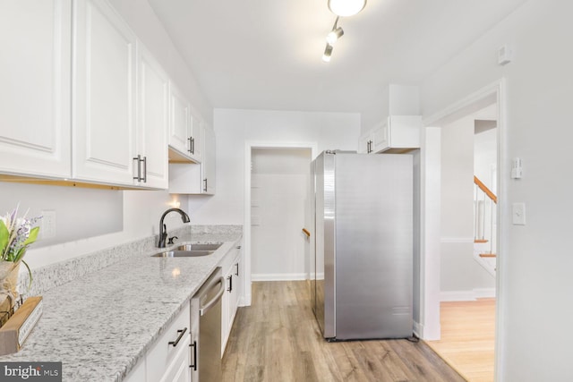 kitchen with a sink, light stone counters, white cabinetry, appliances with stainless steel finishes, and light wood finished floors