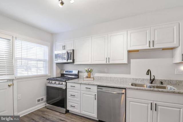 kitchen with a sink, light stone countertops, appliances with stainless steel finishes, white cabinetry, and dark wood-style flooring