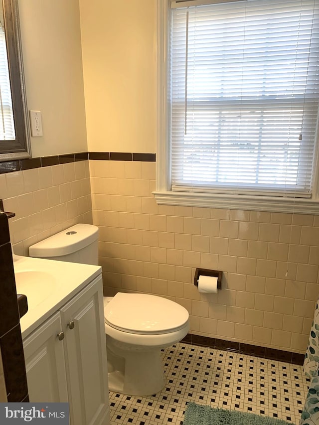 full bath featuring vanity, a wainscoted wall, tile patterned floors, toilet, and tile walls